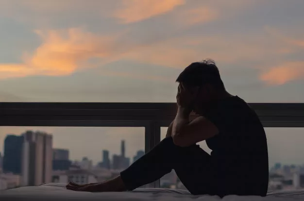 person-sitting-feeling-depressed-bed-with-city-view-dusk-moment_74663-536